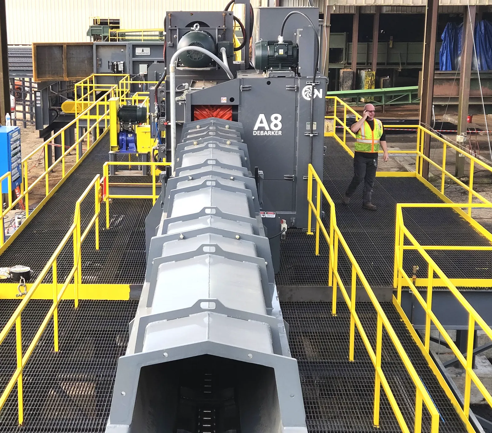 Covered debarker outfeed conveyor running from the A8 debarker toward the trimmer line