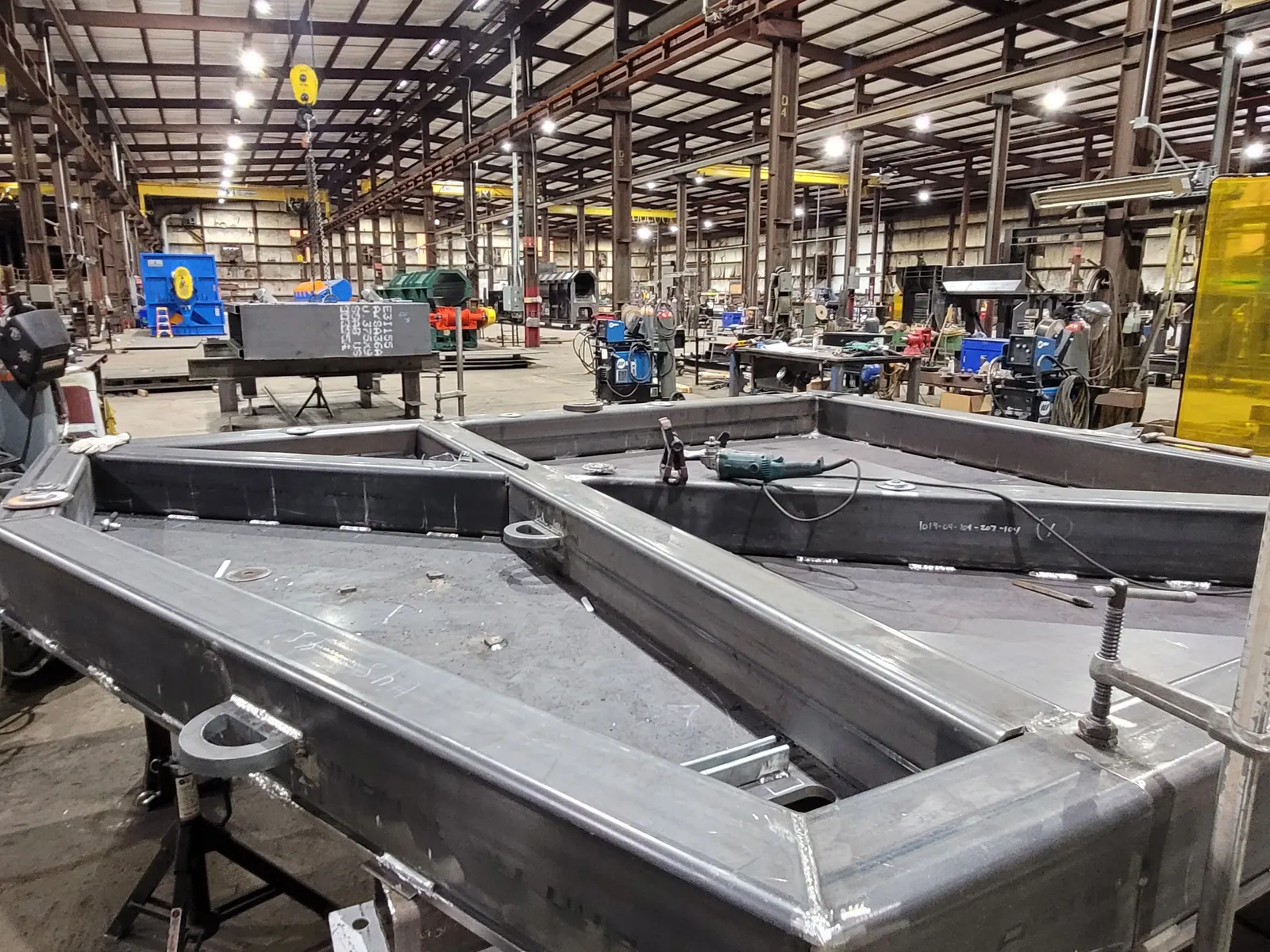 Welded frame assemblies in progress on the shop floor, welding stations behind